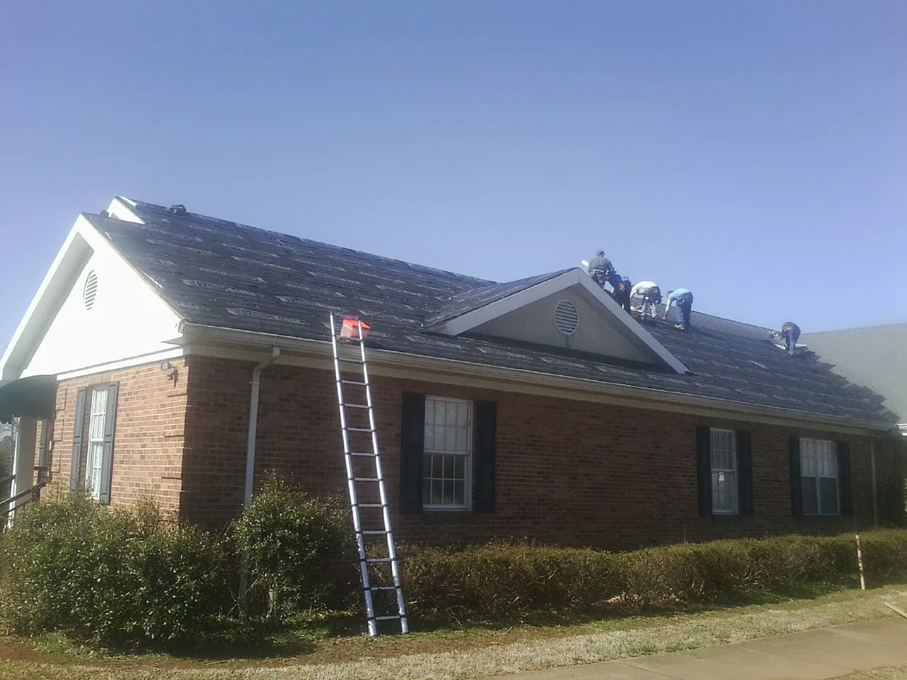 Crew tearing shingles off a brick ranch roof with a ladder set — Emergency Roof Repair work by our crew in Manly