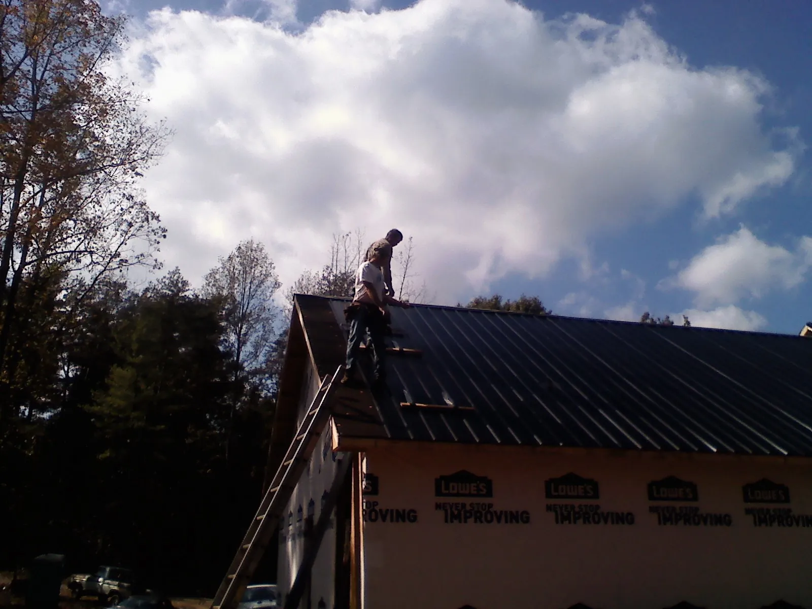 Roofer fastening dark metal panels high against a cloudy sky, from a Roof Inspection job in Manly