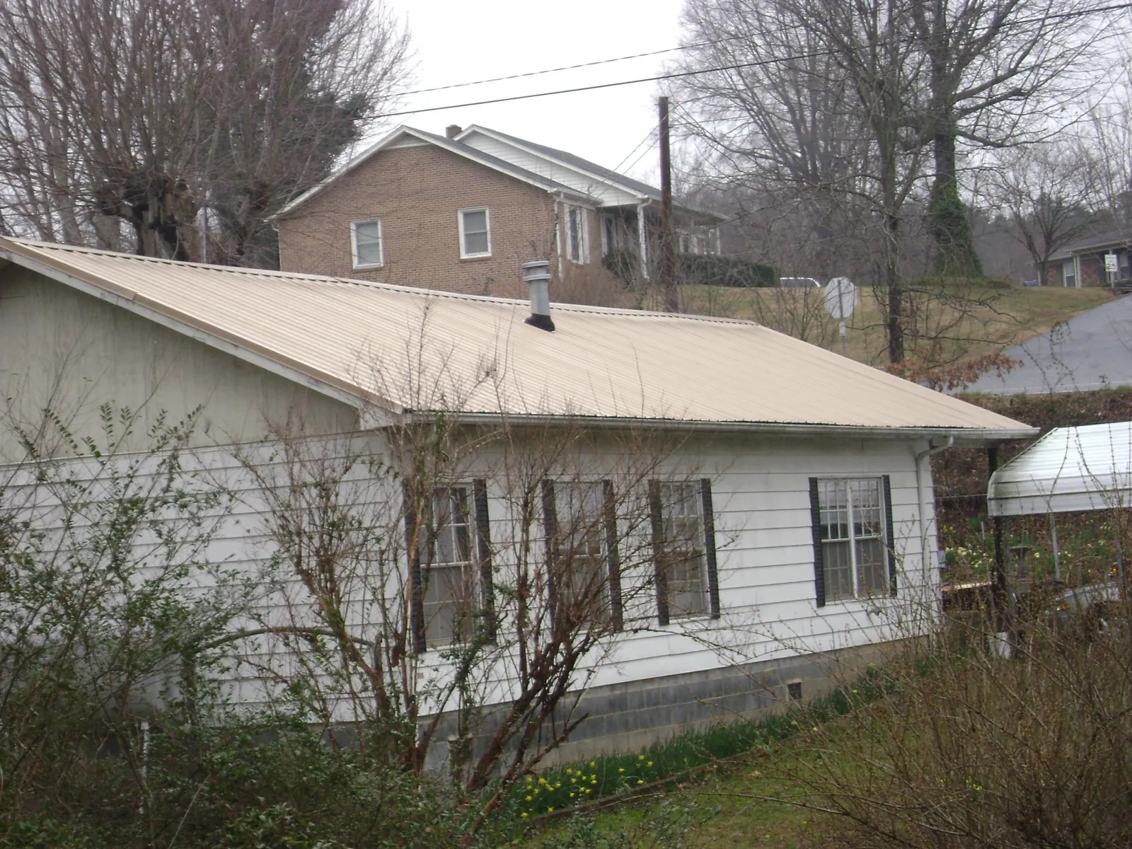 Tan metal roof on a white sided house set into a hillside — Commercial Roofing by Roofing Brothers in Manly